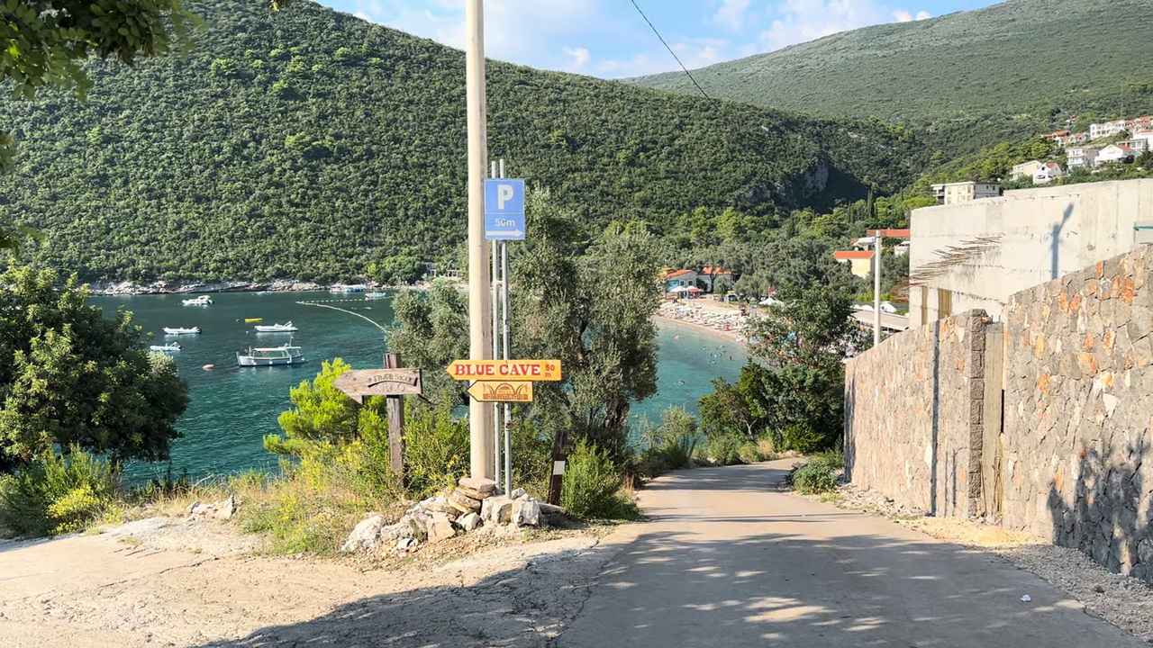 Pogled niz put ka plaži Žanjice, sa morem, čamcima i zelenim brdima u pozadini